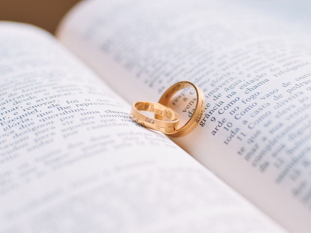 Na otwartych stronach książki leżą dwie złote obrączki ślubne