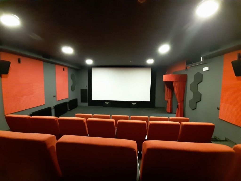 Sala kinowa: ściany w kolorze grafitowym, czerwone fotele, w tle duży biały ekran 