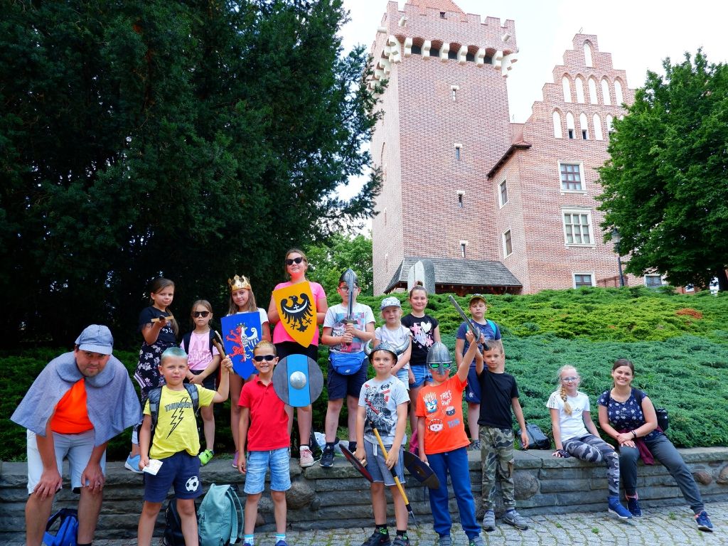 Grupa 15 dzieci stoi przed budynkiem Zamku Przemysła II w Poznaniu