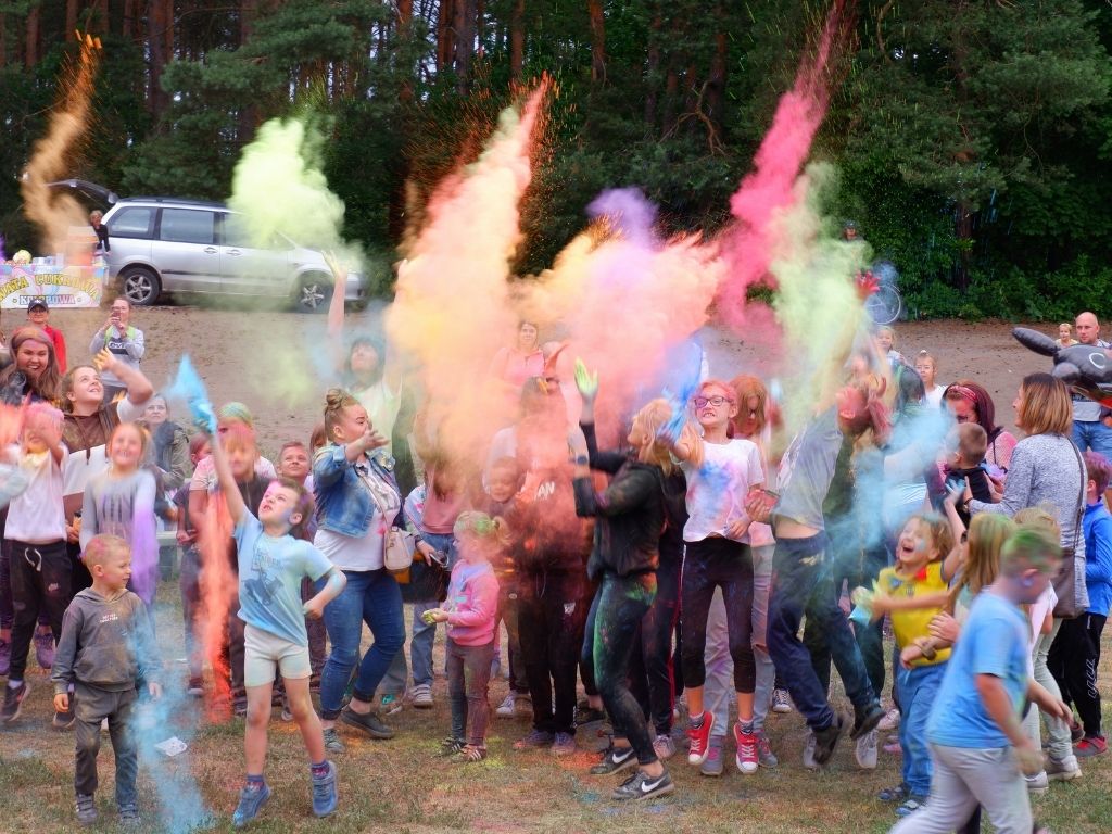 Grupa dzieci wyrzucająca w niebo kolorowe proszki.