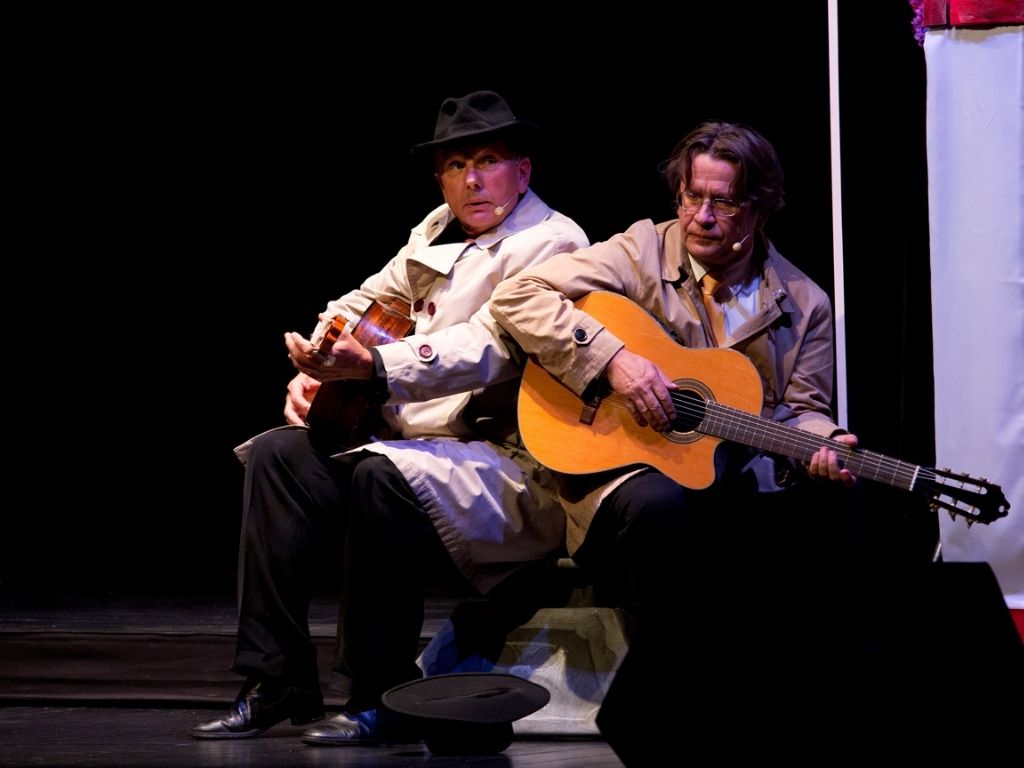 Dwóch mężczyzn grających na gitarze siedzący na krześle.